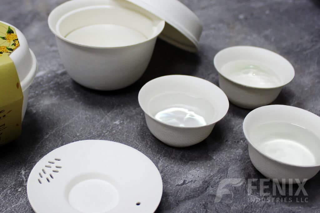 Molded pulp tea cups filled with water on a gray stone surface, demonstrating waterproof performance.